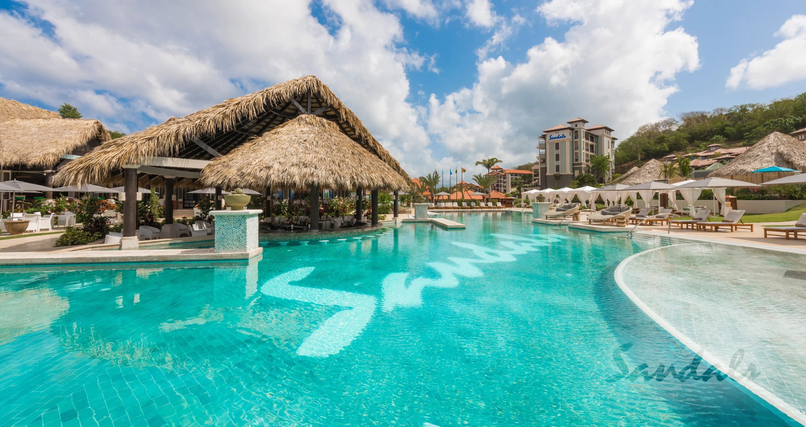 Majestic-pool-on-Saint-George-Island-with-sunbed-canopies-and-a-large-thatch-tiki-hut-nestled-against-a-lush-hillside-scaled.jpeg